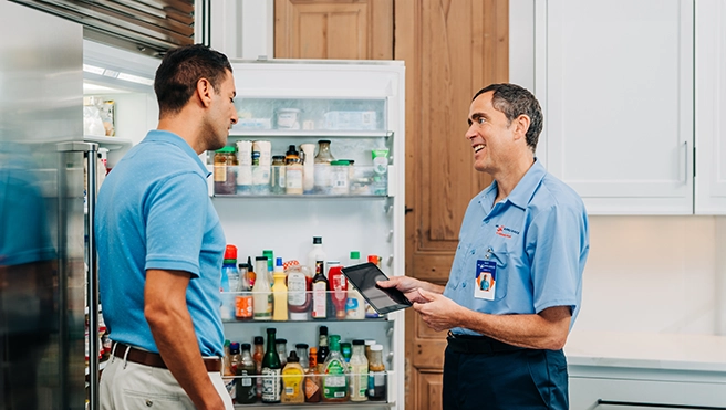 A Mr. Appliance technician talks to a customer in front of an open refrigerator.