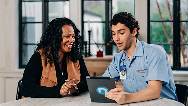 A Mr. Appliance technician talks with a customer while sitting at a table.