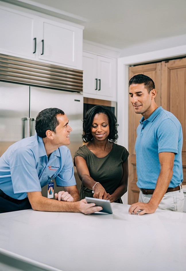A Mr. Appliance technician talks with customers in their kitchen.