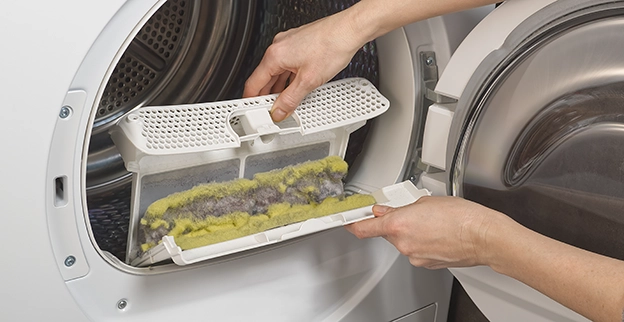 A hand pulling out a full lint trap in a dryer.