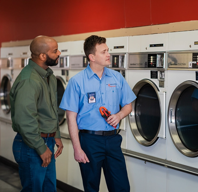 Mr. Appliance service professional looking at row of commercial dryers with customer.