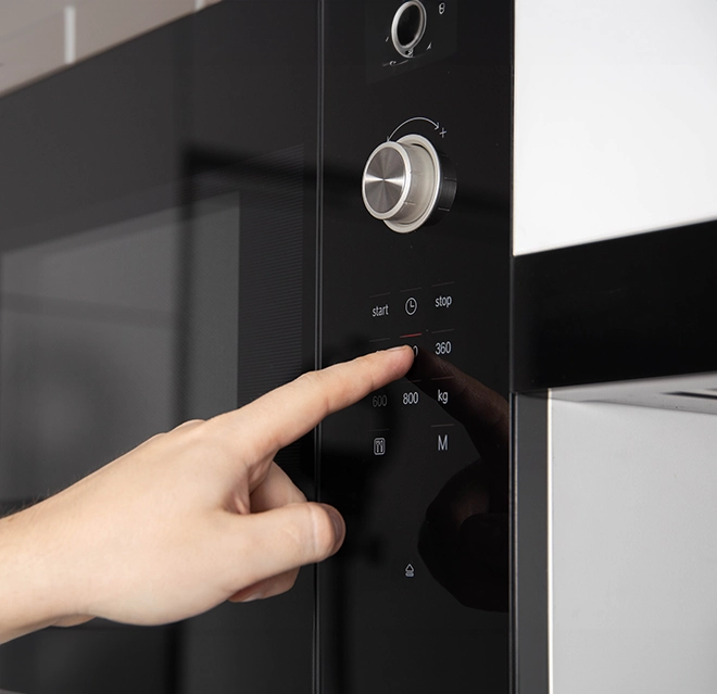 Close up of hand pressing button on black microwave.