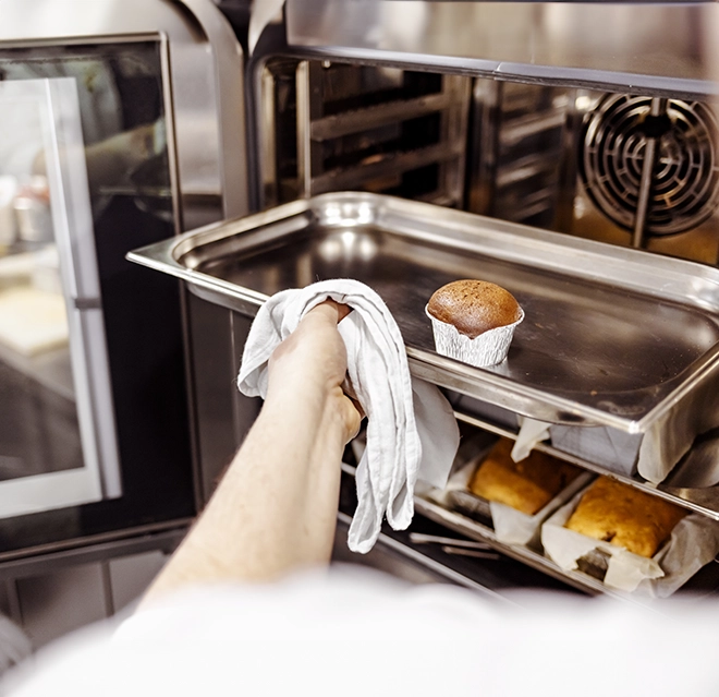 Hand with towel pulling muffing out of commercial oven.