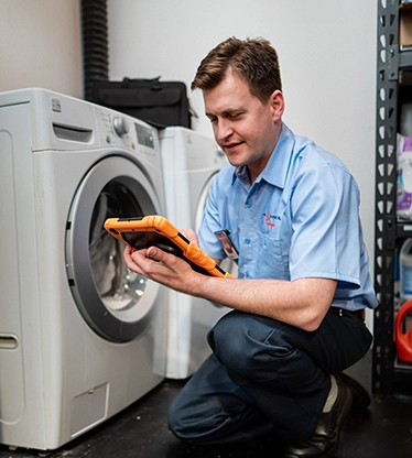 Mr. Appliance service professional reviewing iPad in front of washing machine.