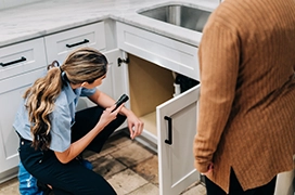 Mr. Appliance service professional shining flashlight underneath sink.
