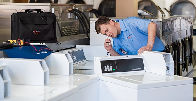 Mr. Appliance service professional inspecting the back of a commercial washing machine.
