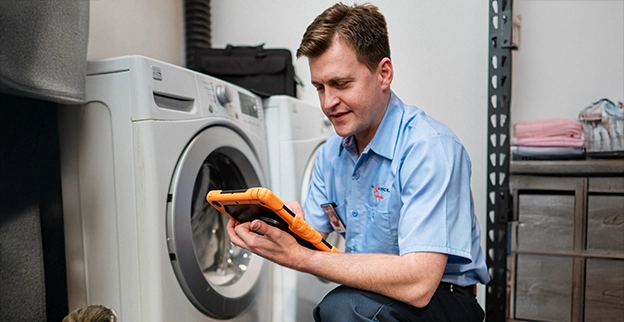Mr. Appliance service professional reviewing iPad in front of washing machine.