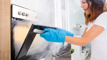 A woman opens an oven with concern on her face and smoke rising out of the appliance.