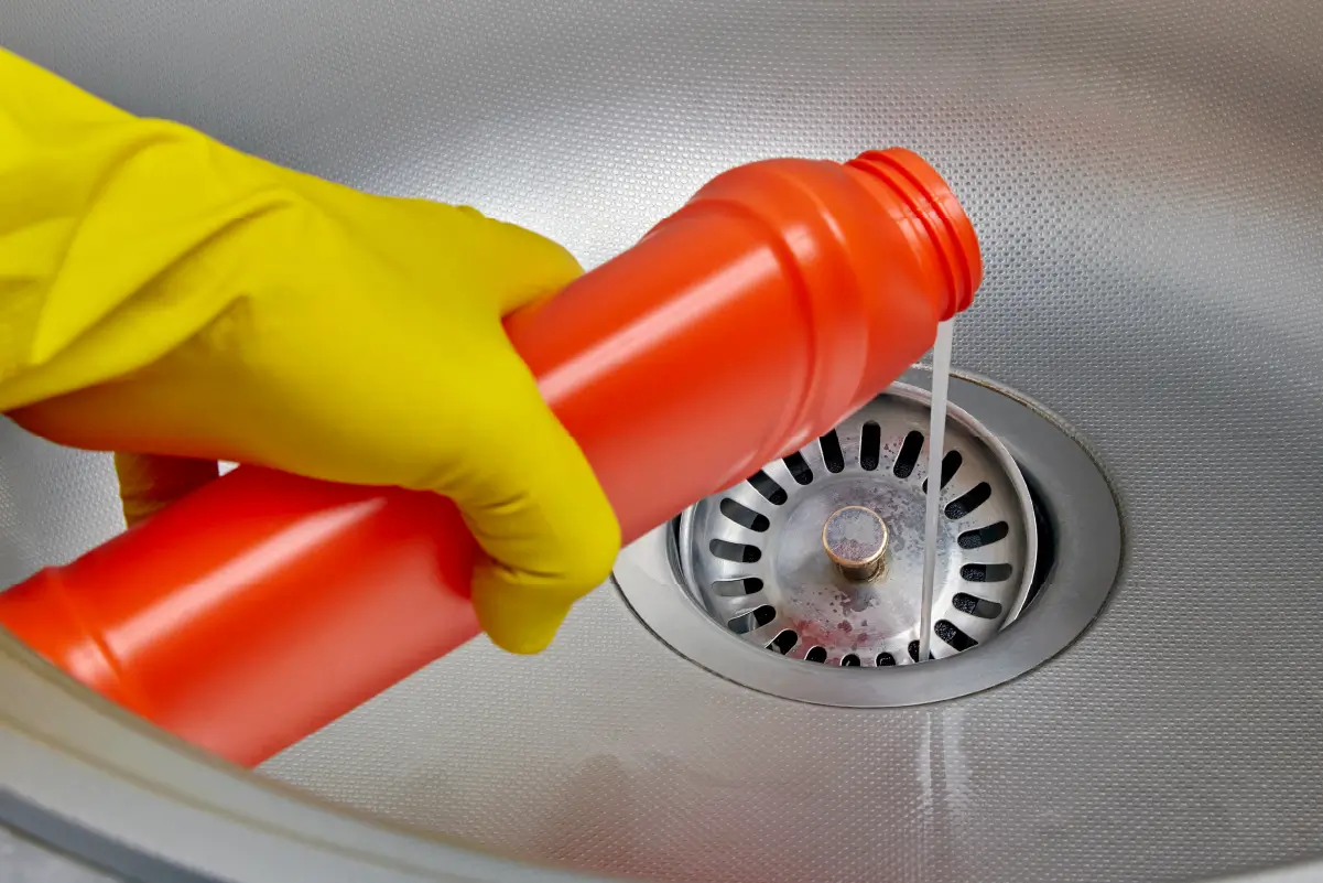 An individual pouring a commercial cleaning solution down a sink.