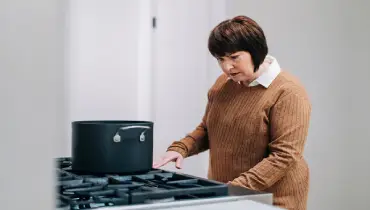 A woman standing at her gas stove trying to start it.