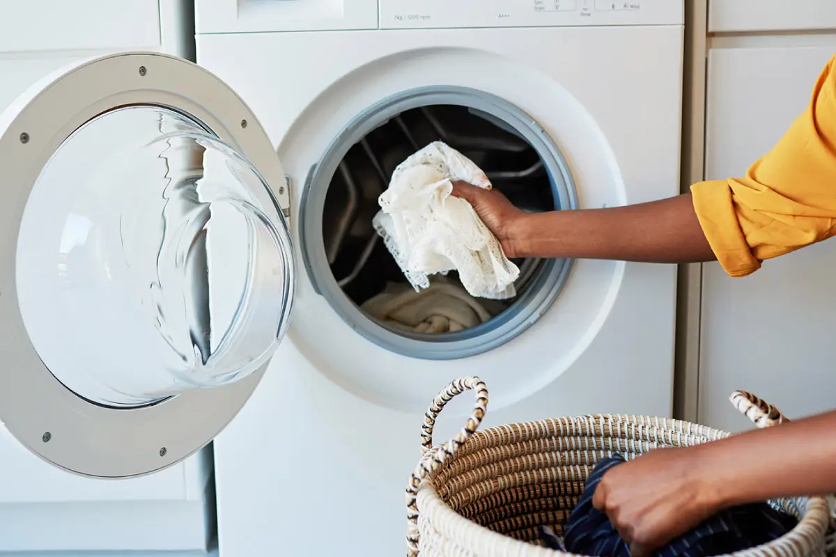 A person putting their clothes into a front-loading washer.