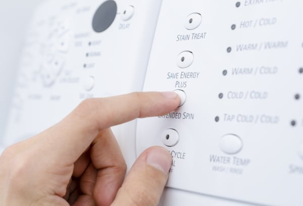 A person's finger pressing a button labeled Save Energy Plus on a washing machine.