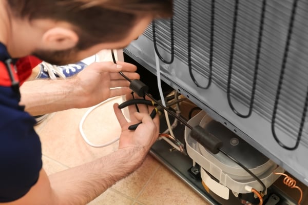Technician working on the back of a refrigerator.
