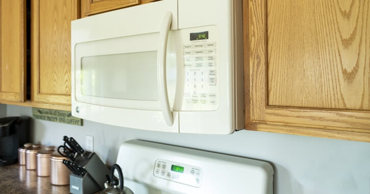 A white microwave built in to the top cabinets in a kitchen.