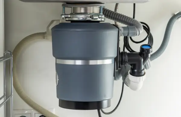 Detail view of a garbage disposal under a kitchen sink with plumbing and electrical connections.