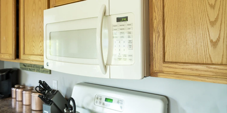 A white microwave built in to the top cabinets in a kitchen.