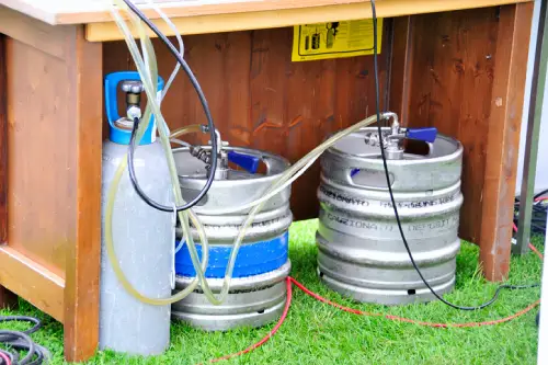 Two metal beer kegs under a table and hooked up to a kegerator system